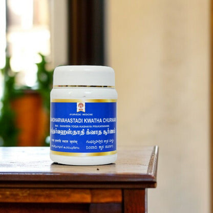 Impcops Gandharva Hastadi Kwatha Churnam Ayurvedic powder in a glass bowl with dried herbs and spices on a white background.