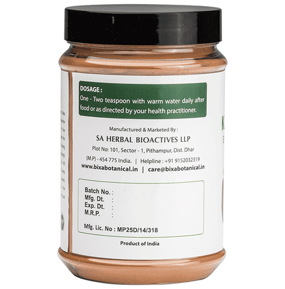 Bixa Botanical Kaiphal Powder in a clear glass jar, showing fine light brown Ayurvedic powder with a wooden spoon.