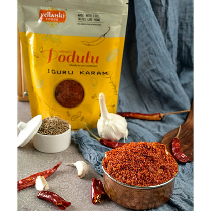 Vellanki Foods Iguru Karam chili powder in a clear glass jar, showing vibrant red chili flakes and seasoning close-up.