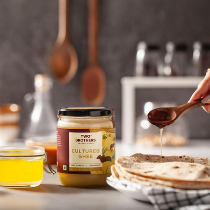 Organic cow ghee butter from Two Brothers Organic Farms, made from grass-fed Gir cows, in a glass jar with a golden hue.