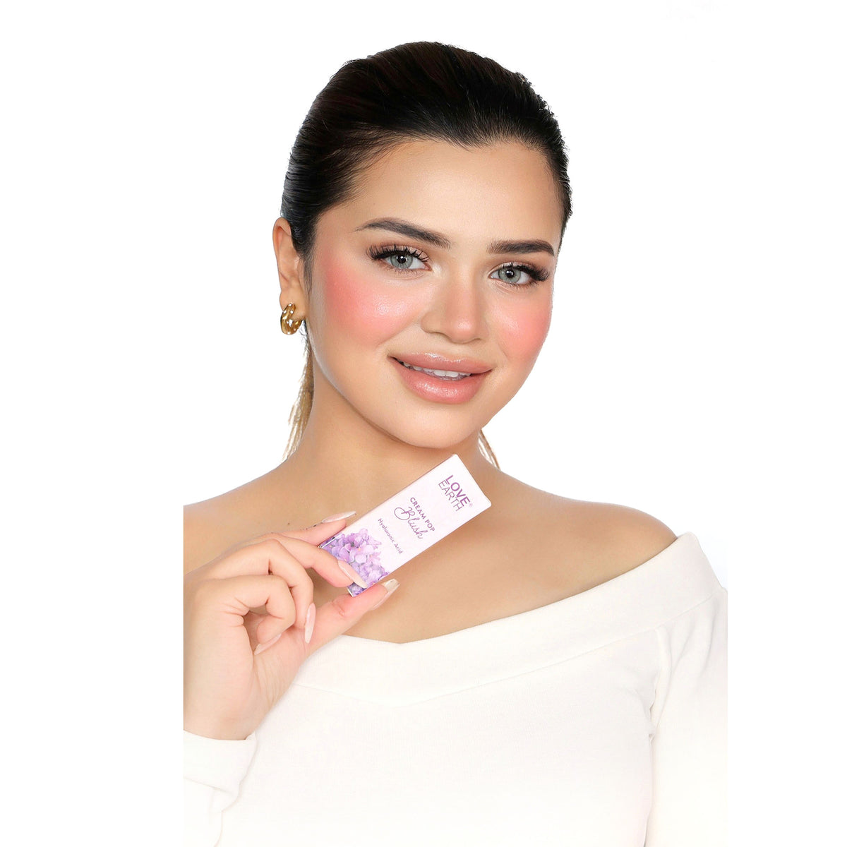 Love Earth Cream Pop Blush in Buttercup showing a compact with peachy-orange blush and a fluffy makeup brush on a neutral background.