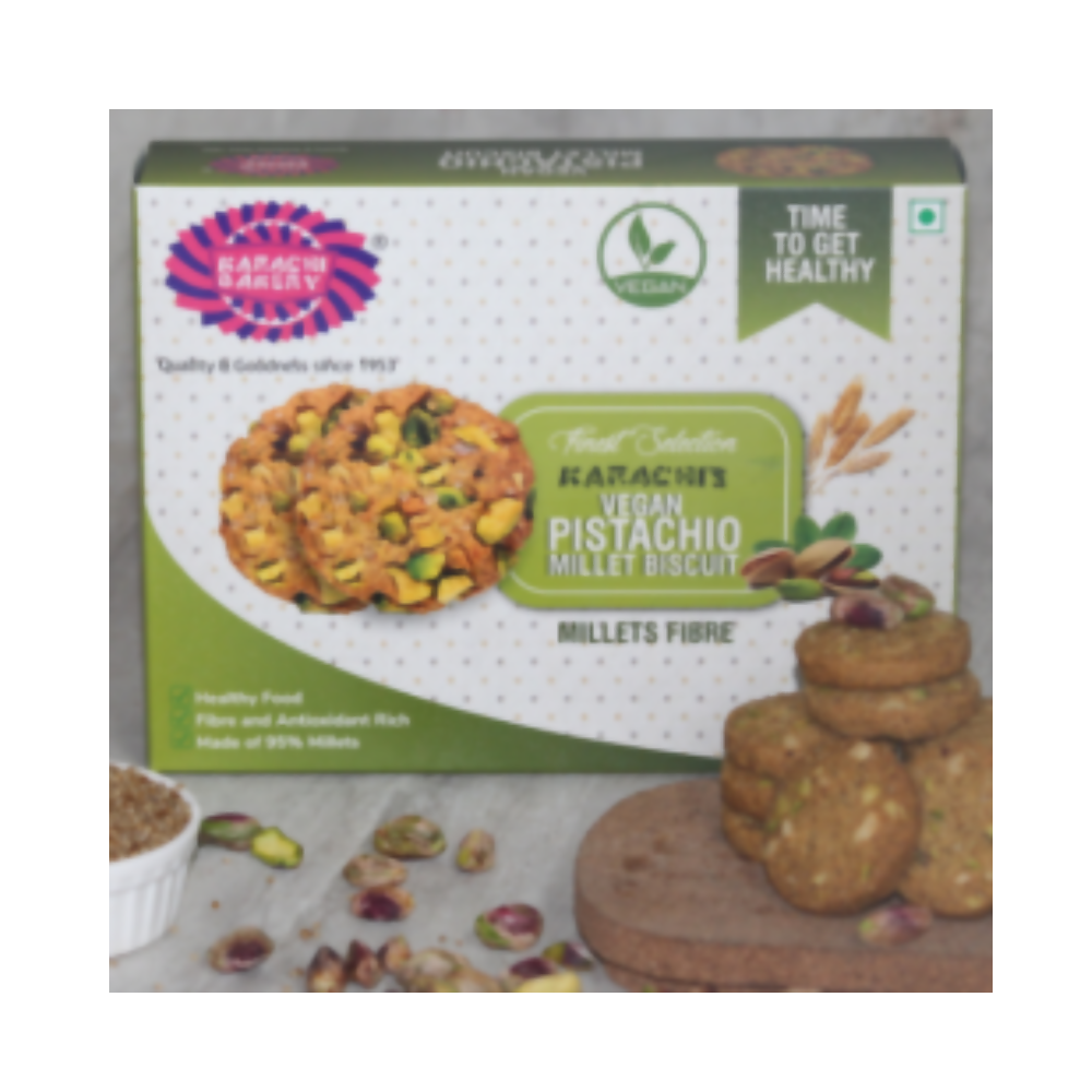 Vegan pistachio millet biscuit from Karachi Bakery, displayed on a white plate with pistachios and millet grains.