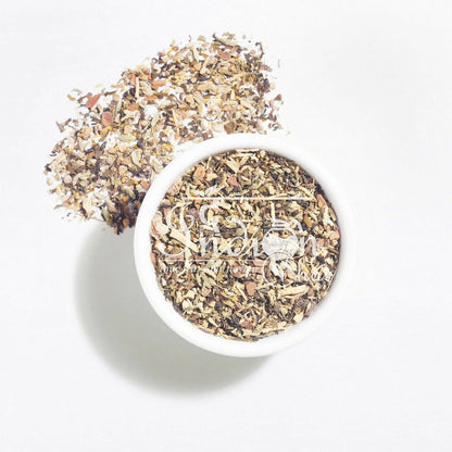 A close-up of The Indian Chai calming Vata Dosha tea powder in a bowl with a tea infuser on a wooden surface.